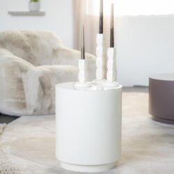 Strakke witte stooklampen op ronde witte tafel in strak modern interieur met zachte stoffen zithoek en lichte gordijnen.