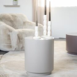 Uitstekende witte kandelaars op ronde wit bijzettafel in modern woonkamer met zacht tapijt en relaxfauteuil, Scandinavisch design, perfecte decoratie voor stijlvolle interieur, Mokana Meubelen.