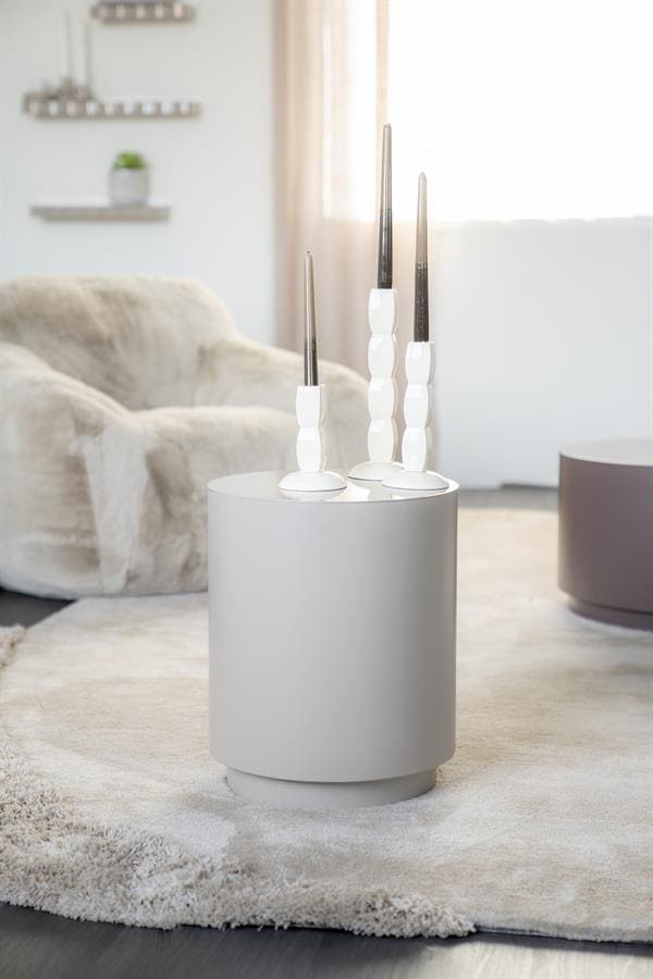 Uitstekende witte kandelaars op ronde wit bijzettafel in modern woonkamer met zacht tapijt en relaxfauteuil, Scandinavisch design, perfecte decoratie voor stijlvolle interieur, Mokana Meubelen.