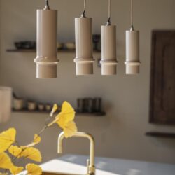 Elegante hanglamp met vier beige keramische lampenkappen, modern design, in een stijlvolle keuken met gouden kraan en natuurlijke decoratie.