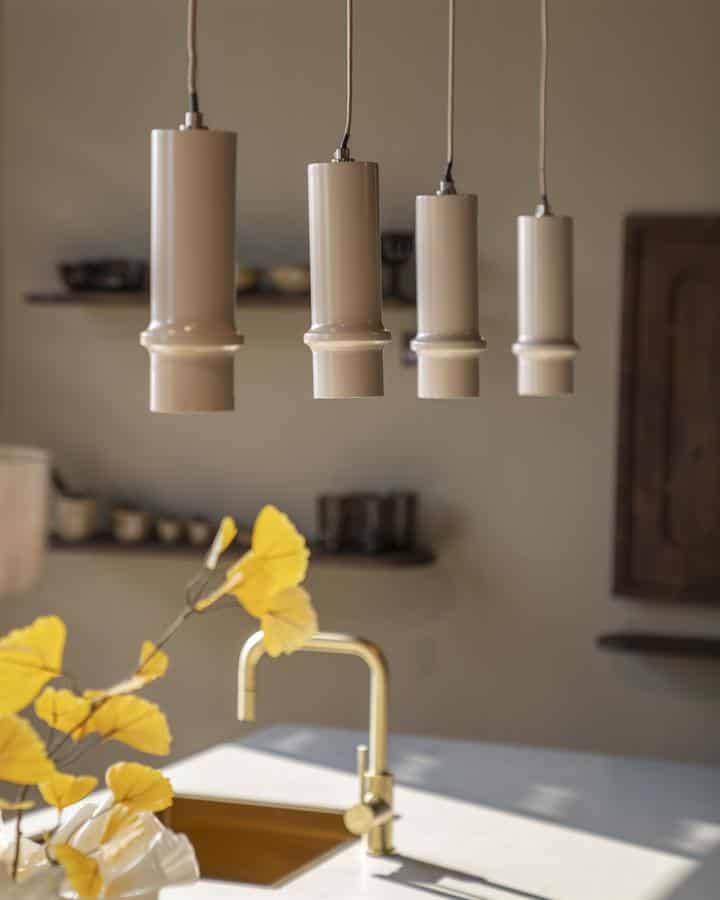 Elegante hanglamp met vier beige keramische lampenkappen, modern design, in een stijlvolle keuken met gouden kraan en natuurlijke decoratie.