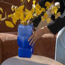 Blauwe glazen vaas met gele bloemen, modern interieur, Mokana Meubelen, designwoonaccessoires, stijlvolle inrichting, handgemaakte decoraties, unieke meubelstukken, elegant woonidee, interieur styling, woondecoratie, lounge meubelen, designaccessoires, Dutch design.