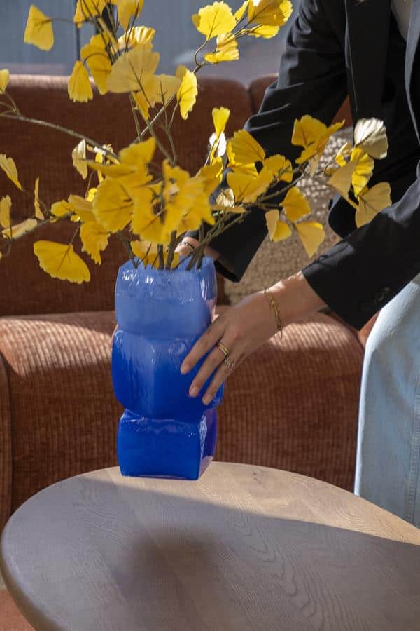 Blauwe glazen vaas met gele bloemen, modern interieur, Mokana Meubelen, designwoonaccessoires, stijlvolle inrichting, handgemaakte decoraties, unieke meubelstukken, elegant woonidee, interieur styling, woondecoratie, lounge meubelen, designaccessoires, Dutch design.