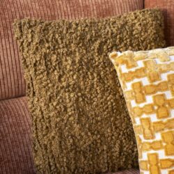 Knusse oranje sofa met twee sierkussens, een met een wollige textuur en een met een geometrisch patroon, in een gezellige woonkamer, perfect voor comfortabele ontspanning en stijlvol wonen.