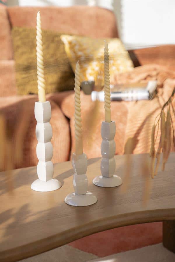 Stijlvolle witte en beige waxinelichthouders met gedraaide kaarsen op een houten salontafel in een gezellige woonkamer.