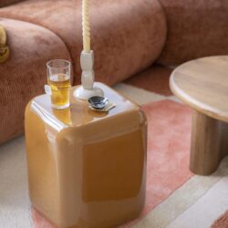 Unieke gele opbergpoef in modern interieur met kaars, glas bier en horloges, perfect voor multifunctioneel gebruik als salontafel en stoere decoratie.