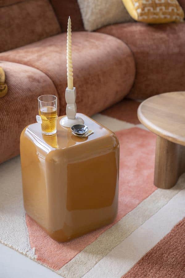 Unieke gele opbergpoef in modern interieur met kaars, glas bier en horloges, perfect voor multifunctioneel gebruik als salontafel en stoere decoratie.