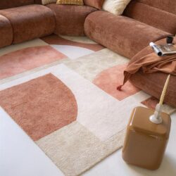 Rustkleurige stoffen hoekbank met sierkussens in neutrale tinten, gestyled in een moderne woonkamer met een abstract geometrisch tapijt, perfect voor gezellige en stijlvolle zithoeken.