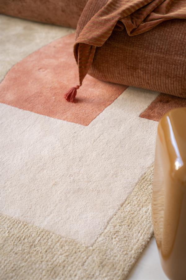 Kunstleren tapijt in beige en roze tinten met zachte textuur, gelegen naast een reliëfstoel en gestoffeerde bank, ideaal voor een stijlvolle en gezellige woonkamer inrichting.