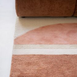 Leuke landelijke warme hoekbank met een kleurtje van terracotta en lichtroze, en een zachte wollen vloerkleed in pastel tinten. Een gezellig en comfortabel zitgedeelte met natuurlijk houten vloer.