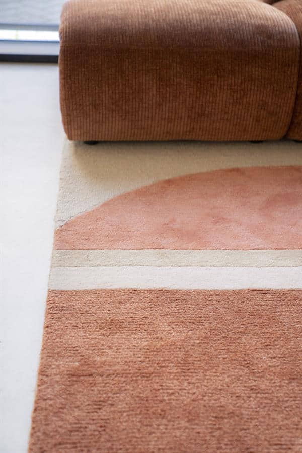 Leuke landelijke warme hoekbank met een kleurtje van terracotta en lichtroze, en een zachte wollen vloerkleed in pastel tinten. Een gezellig en comfortabel zitgedeelte met natuurlijk houten vloer.