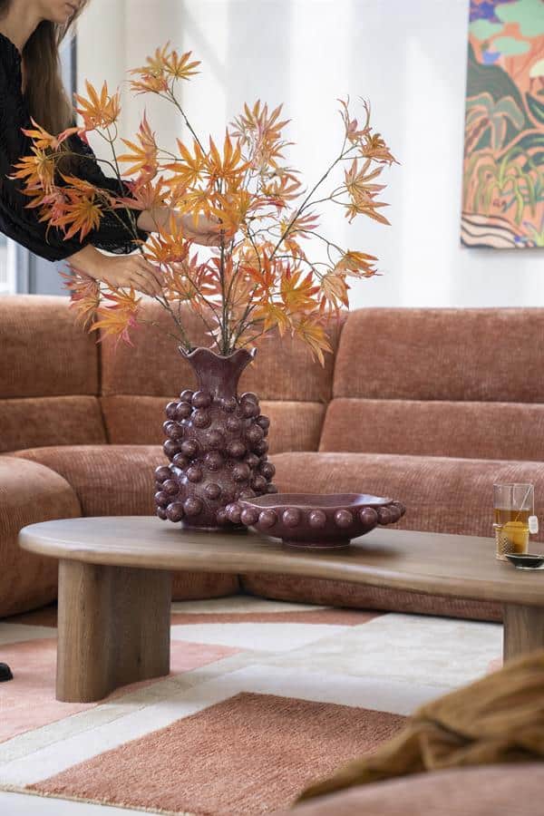 Bladvormige bladeren in een vaas op een houten salontafel in een modern woonkamer met een blushroze bank en abstract kunstwerk op de muur.