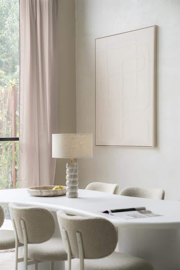 Minimalistisch eettafel met moderne lamp en zachte keukenstoelen in een lichte, sfeervolle woonkamer met natuurlijke lichtinval.