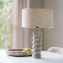 Lamp met gemarmerd houten voet en beige stoffen kap op een wit tafelblad in een modern interieur.