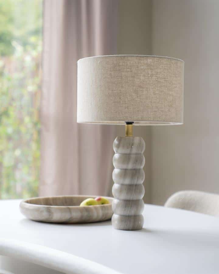 Lamp met gemarmerd houten voet en beige stoffen kap op een wit tafelblad in een modern interieur.