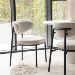 Eetkamerstoelen met zwart metalen poten en lichtgrijze bekleding, plaatsen rondom een wit eettafel met raam en tuinzicht, modern en sfeervol interieur.
