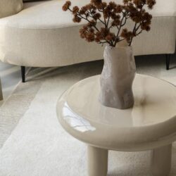 Modern elegante vaas met gedraaide vorm op een minimalistisch witte bijzettafel in een woonkamer, gecombineerd met zachte stoffen banken en decoratieve kussens.