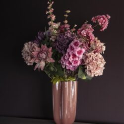 Zijden bloemen in roze en paarstinten in keramische vaas op donkergrijze achtergrond.