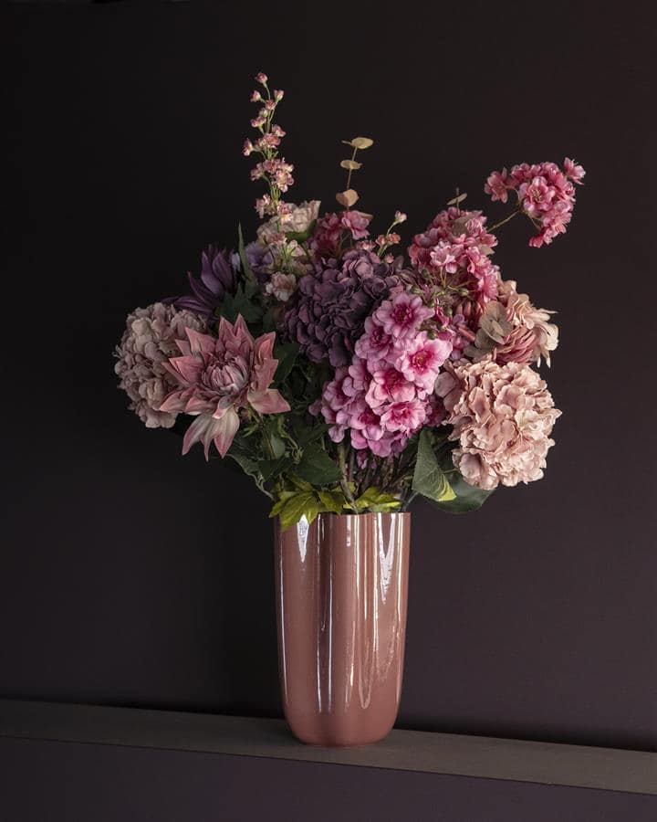 Zijden bloemen in roze en paarstinten in keramische vaas op donkergrijze achtergrond.