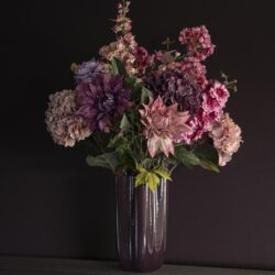 Bloemstuk in paarse glazen vaas met roze en purple bloemen op donkere achtergrond.