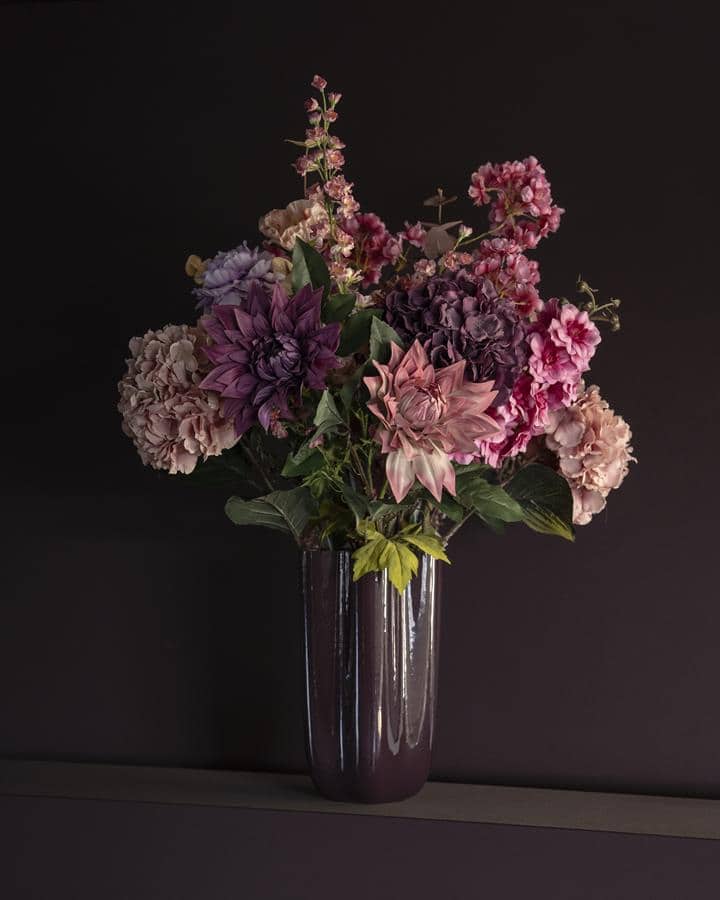 Bloemstuk in paarse glazen vaas met roze en purple bloemen op donkere achtergrond.