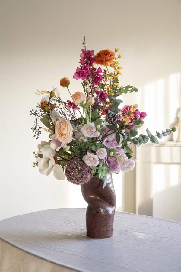 Gevarieerd boeket bloemen in mooie keramieke vaas op tafel, elegant bloemstuk voor interieur decoratie, Mokana Meubelen, stijlvolle bloemenvaas, modern woonaccessoire, bloemstuk voor woninginrichting, kleurrijke bloemenarrangementen, inspiratie voor huisdecoratie, exclusieve bloemenvaas collectie, lachen met bloemen, elegant woonidee, bloemenstyling for home decor.