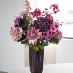 Zwarte wijnfles vaas met een kleurrijk boeket van roze, paarse en witte bloemen, ideaal voor huisdecoratie en stijlvolle meubels.