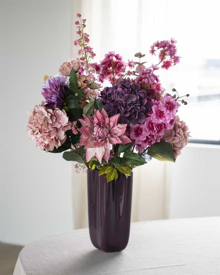 Zwarte wijnfles vaas met een kleurrijk boeket van roze, paarse en witte bloemen, ideaal voor huisdecoratie en stijlvolle meubels.
