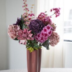 Roze en paarse bloemen in een metallic roze vaas op een witte tafel, ideaal voor stijlvolle interieurdecoratie.