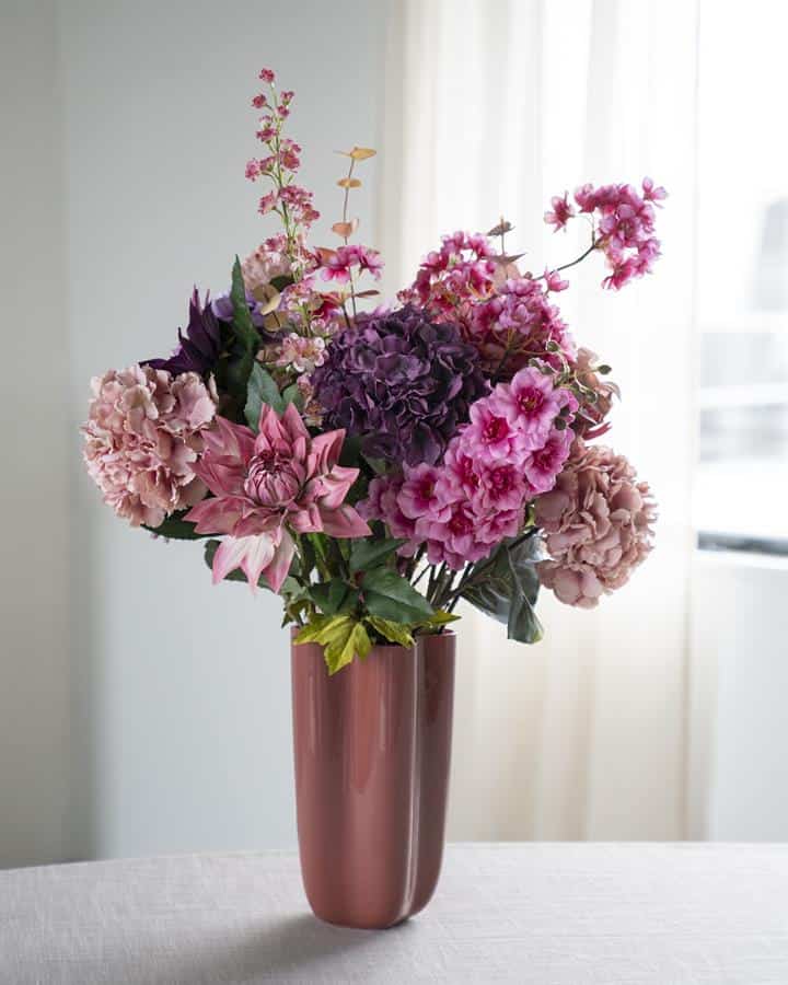 Roze en paarse bloemen in een metallic roze vaas op een witte tafel, ideaal voor stijlvolle interieurdecoratie.