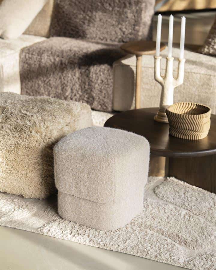 Fluwelen poef in crèmetinten als stijlvol en veelzijdig meubelstuk voor een gezellige zithoek.