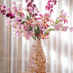 Donkerroze en lichtroze bloemen in keramische vaas op houten tafel met gordijnen achtergrond.