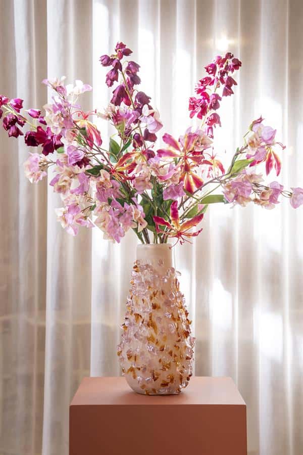 Donkerroze en lichtroze bloemen in keramische vaas op houten tafel met gordijnen achtergrond.