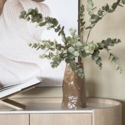 Rustieke keramische vaas met eucalyptus takken op een lichte houten meubel, elegant woningdecor, Mokana Meubelen, stijlvolle interieuraccessoires, natuurlijke sfeer, moderne en tijdloze inrichting.