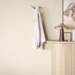 Stijlvolle witte handdoek aan wandhaak boven een beige houten console met decoratieve lamp, in een moderne woonkamer.