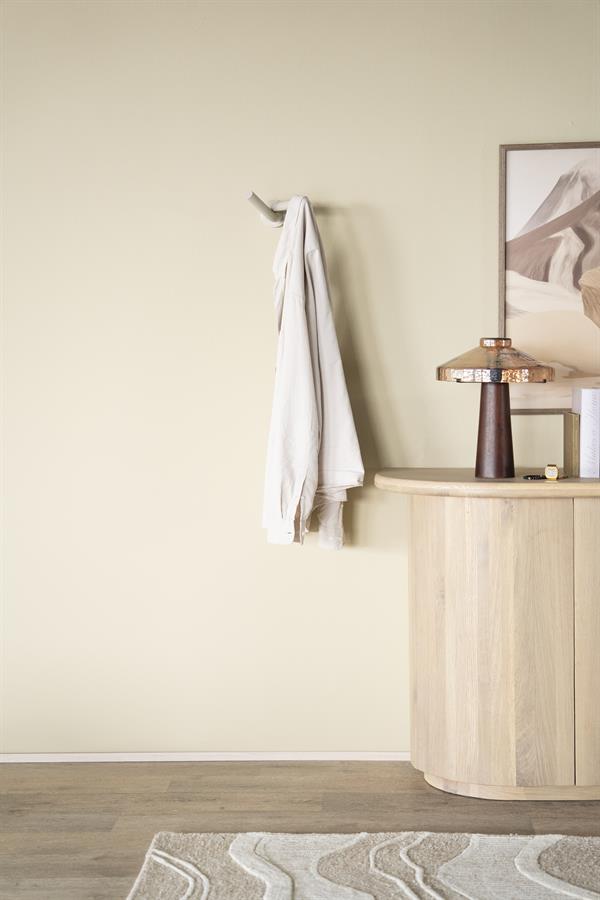 Stijlvolle witte handdoek aan wandhaak boven een beige houten console met decoratieve lamp, in een moderne woonkamer.