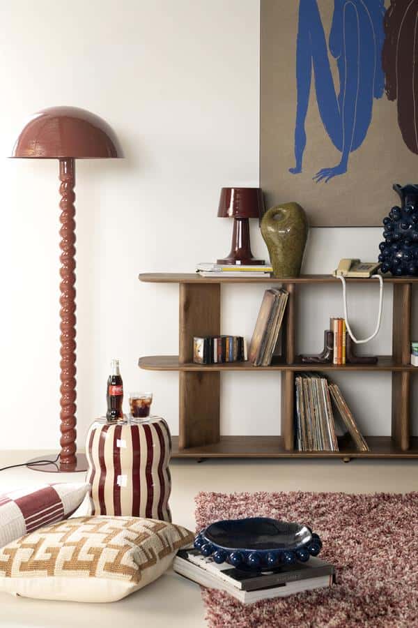 Unieke vintage houten boekenkast met moderne accessoires, stijlvolle vloerlamps, en comfy kussens in een gezellige woonkamer. Perfect voor een warm en eigentijds interieur door Mokana Meubelen.