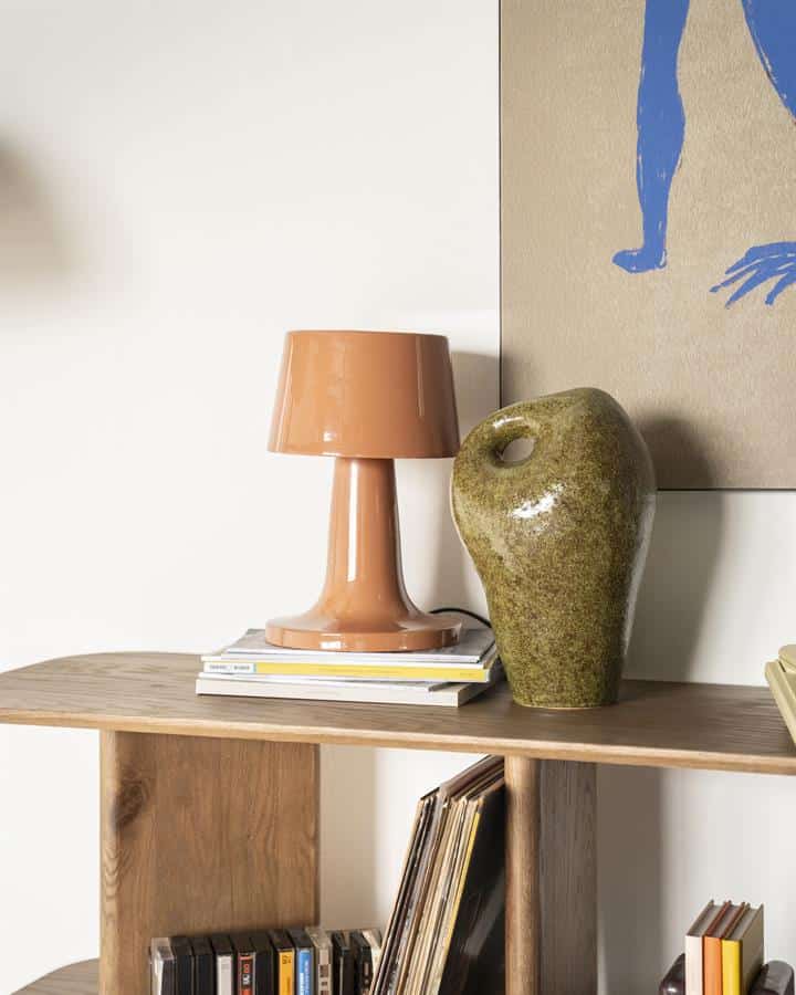 Stijlvolle keramische vaas en moderne tafellamp op houten boekenkast in minimalistische woonkamer, perfect voor een warme en gezellige interieurstyle met natuurlijke materialen.