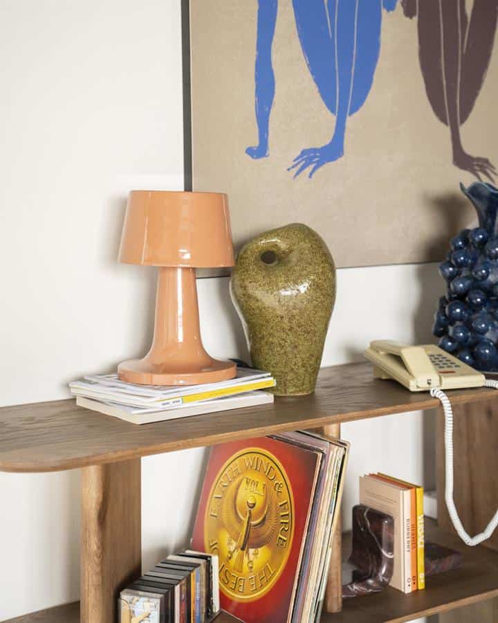 Elegante houten wandplank met diverse decoratieve items zoals een keramische vaas, een boekenrek met vinylplaten en een vintage telefoon, ideaal voor een stijlvolle en functionele inrichting.