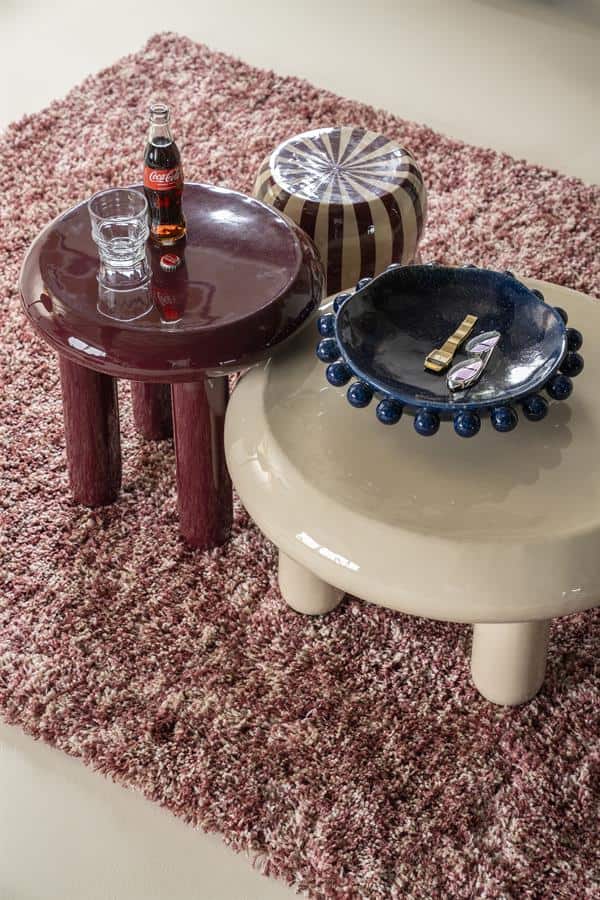 Houten bijzettafels in verschillende kleuren en stijlen op een zachte, roze tapijtrug, perfect voor modern interieur en woonaccessoires.