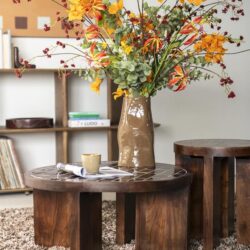Kunstbloemen in een vaas op een houten salontafel, modern interieur met boekenkast en kunstwerk op de achtergrond. Perfect voor een gezellige woonkamerdecoratie.