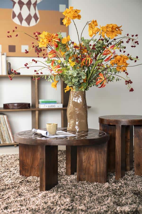 Kunstbloemen in een vaas op een houten salontafel, modern interieur met boekenkast en kunstwerk op de achtergrond. Perfect voor een gezellige woonkamerdecoratie.