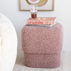 Kleurrijk/upholstered, pastel roze, zachte poef van Mokana Meubelen met boeken en glas op, moderne woonkamer decoratie, comfortabel en trendy design.