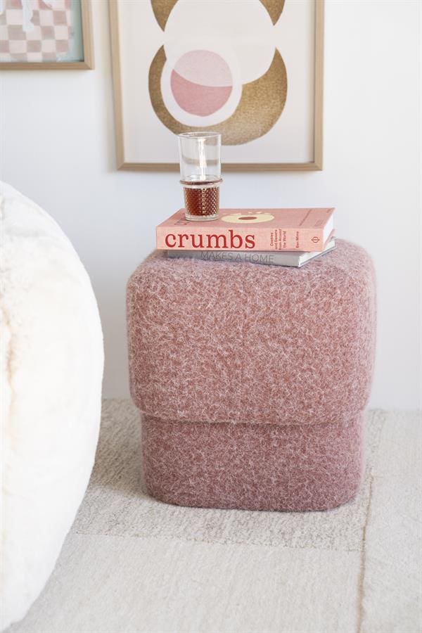 Kleurrijk/upholstered, pastel roze, zachte poef van Mokana Meubelen met boeken en glas op, moderne woonkamer decoratie, comfortabel en trendy design.