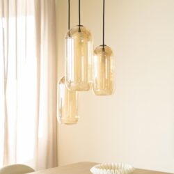 Strakke moderne hanglamp met vier amberkleurige glazen kappen boven eettafel. High-end design verlichting, perfect voor hedendaagse interieurs.