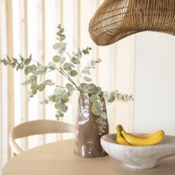 Rustieke vaas met eucalyptus op een houten eettafel, moderne interieurdecoratie met natuurlijke materialen en pastelkleuren, sfeervol en stijlvol.