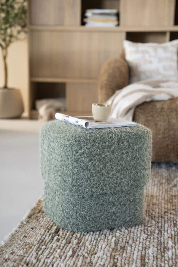 Knusse groene poef van vloerkleedstof in een moderne woonkamer met natuurlijke houten elementen en comfortabele zithoek. Perfect voor gezellige, Scandinavische interieurstijl.