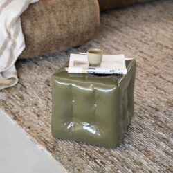 Kunststof bijzettafel in olijfgroene kleur met ingedrukte details, op een tapijtvloer naast een beige bank met een plaid, perfect voor een modern interieur.