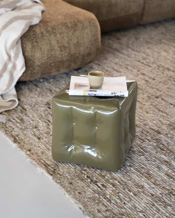 Kunststof bijzettafel in olijfgroene kleur met ingedrukte details, op een tapijtvloer naast een beige bank met een plaid, perfect voor een modern interieur.