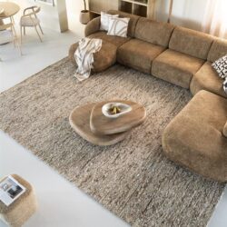 Knusse hoekbank in warm beige stoffen bekleding met bijpassende sierkussens, houten salontafel en moderne interieurdecoratie, perfect voor een stijlvolle woonkamer.